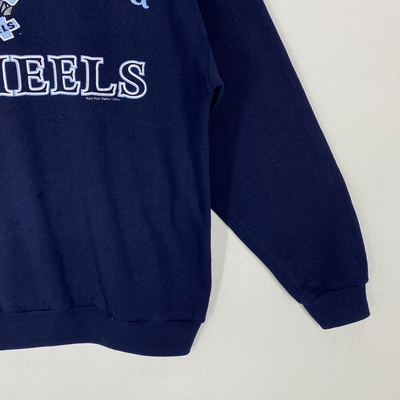 May include: Navy blue sweatshirt featuring the word "HEELS" in large white block letters. The sweatshirt has a crew neck and long sleeves. The text "Run Run Rules 1254" is below the word "HEELS".