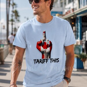 Puede incluir: Una camiseta azul claro con un gr&aacute;fico de una mano pintada con el dise&ntilde;o de la bandera canadiense, mostrando el dedo medio. Debajo del gr&aacute;fico, el texto TARIFF THIS est&aacute; impreso en una fuente negra, negrita y con efecto desgastado.