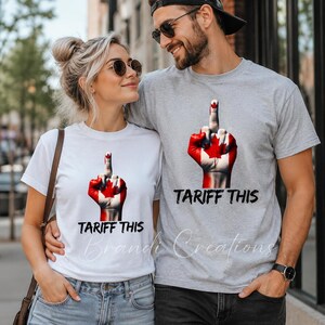 Puede incluir: Una camiseta blanca y una camiseta gris jaspeado, cada una con un gr&aacute;fico de una mano pintada con la bandera canadiense haciendo un gesto de dedo medio, con el texto TARIFF THIS impreso en letras negras debajo del gr&aacute;fico en ambas.