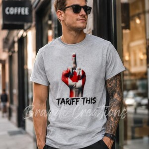 Puede incluir: Una camiseta gris jaspeado de manga corta con un gr&aacute;fico de una mano pintada con el dise&ntilde;o de la bandera canadiense, mostrando el dedo medio. Debajo del gr&aacute;fico, el texto TARIFF THIS est&aacute; impreso en una fuente negra, negrita y desgastada.