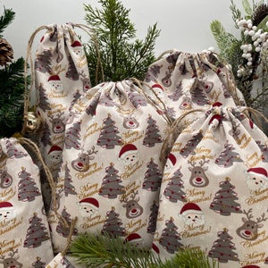 Könnte beinhalten: Satz von sechs beigefarbenen Kordelzugbeuteln mit Weihnachtsmotiv. Die Beutel zeigen ein sich wiederholendes Muster aus Rentieren, Weihnachtsmann und Weihnachtsbäumen mit Lichtern. Der Text "Merry Christmas!" ist in Gold auf den Beuteln gedruckt.