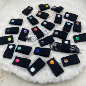 Könnte beinhalten: Sortiment an bunten Kabelbindern mit schwarzem Filz und verschiedenen farbigen Knöpfen. Die Bänder dienen zum Organisieren und Ordnen von Kabeln und Leitungen.