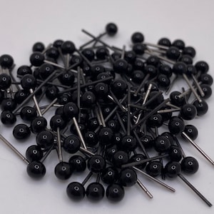 May include: A large pile of black plastic safety eyes with silver metal pins. The eyes are all the same size and are arranged in a random pattern.