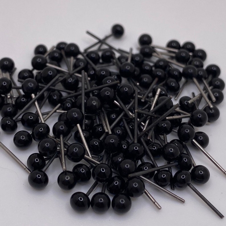 May include: A large pile of black plastic safety eyes with silver metal pins. The eyes are all the same size and are arranged in a random pattern.
