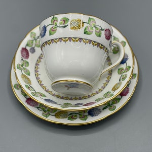 Może przedstawiać: Biały zestaw filiżanki i spodeczka do herbaty z kwiatowym wzorem w odcieniach różowego, żółtego, zielonego i niebieskiego. Zestaw ma złotą obwódkę.