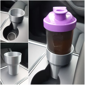 May include: A purple and gray shaker bottle with a lid and a gray cup holder. The bottle is sitting in the cup holder, which is attached to a gray surface.