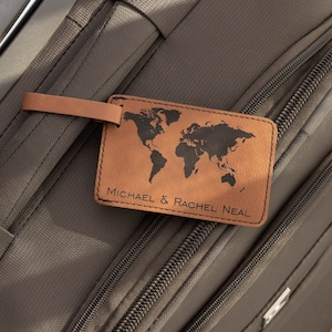 May include: Brown leather luggage tag with a world map design and the text "MICHAEL & RACHEL NEAL" attached to a brown suitcase.