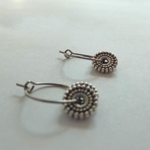 Könnte beinhalten: Ein Paar silberne Creolen mit einem runden Design. Die Ohrringe bestehen aus kleinen Perlen, die in einem Kreis angeordnet sind. Die Ohrringe sind ein schlichtes und elegantes Design.