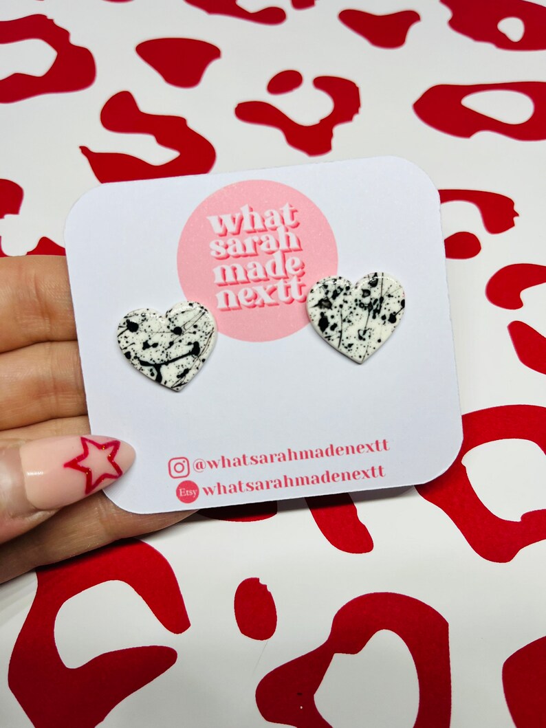 White and black paint splatter larger heart polymer clay stud earrings on stainless steel butterflies.