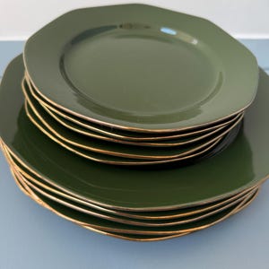 Może przedstawiać: Stos zielonych talerzy ze złotym obramowaniem. Talerze mają nietypowy, lekko nieregularny kształt. Talerze są ułożone jeden na drugim, prezentując wzór i kolor. Każdy talerz ma średnicę około 20 cm.