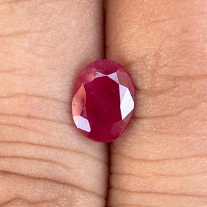 May include: A deep red oval-shaped gemstone with a faceted cut.