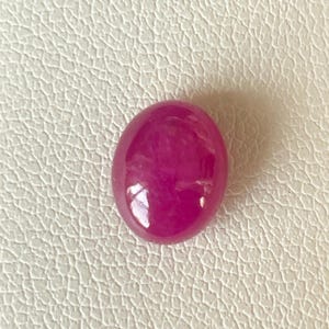Pode incluir: Uma gema oval de cor rosa vibrante com uma superfície lisa e polida.