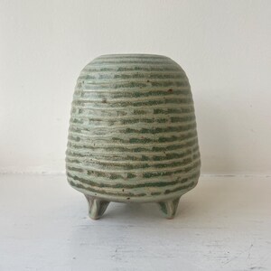Op de afbeelding: Een kleine, groene keramische vaas met een geribbeld ontwerp en drie poten.
