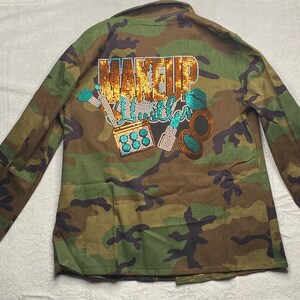 May include: Camouflage green jacket with a sparkly gold and turquoise design that says "Makeup Killer" on the back.