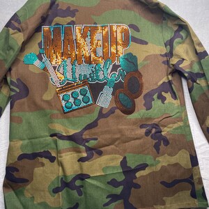 May include: Camouflage green utility jacket with a rhinestone design that says "Makeup Unleashed".