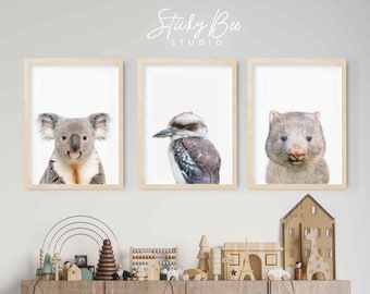 May include: Three framed prints of Australian animals, a koala, a kookaburra, and a wombat, are displayed on a white wall above a wooden shelf with toys. The shelf is above a wooden cabinet with a white rabbit nightlight in front of it. A black and white road rug is on the floor.