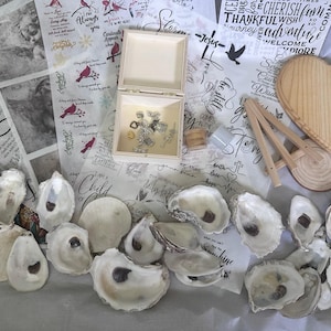 Könnte beinhalten: Eine Auswahl an dekorativen Gegenständen, darunter offene Austernschalen, ein Holzherz, eine kleine Holzbox mit Schmuck und bedrucktes Papier mit inspirierenden Zitaten und Vogelillustrationen. Ein kleiner Holzstaffelei ist ebenfalls vorhanden.