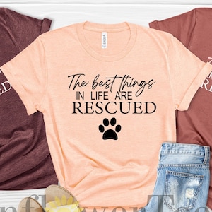 May include: Three t-shirts with the text "The best things in life are rescued" and a paw print. The shirts are in maroon, peach, and mauve.