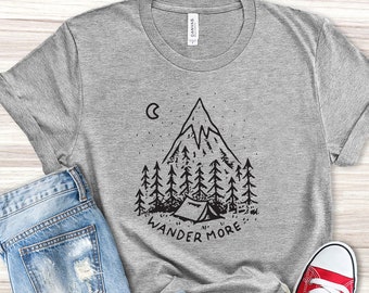 May include: A light grey heather t-shirt with a black and white graphic of a mountain, trees, a crescent moon, and a tent. The text "Wander More" is below the graphic.