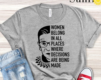 May include: A light grey heather t-shirt with a black and white illustration of Ruth Bader Ginsburg and the text "Women belong in all places where decisions are being made".