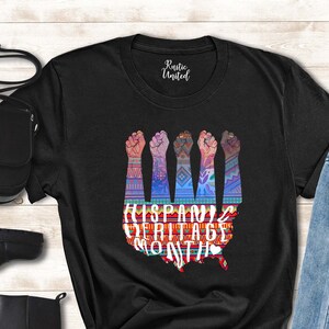 May include: Black t-shirt with a graphic of raised fists forming the shape of the United States. The graphic is colorful and includes the text "Hispanic Heritage Month".