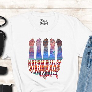 May include: White t-shirt with a graphic of five raised fists in front of a colorful map of the United States. The text "HISPANIC HERITAGE MONTH" is printed below the graphic.