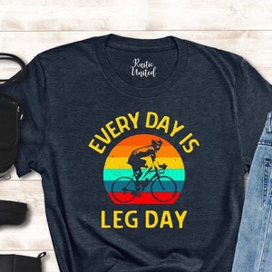 May include: A dark blue t-shirt with a vintage-style graphic of a person riding a bicycle with the text "Every Day Is Leg Day".
