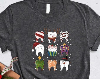 May include: A dark gray t-shirt with a design of white teeth wearing various holiday-themed hats and accessories. The teeth are wearing a Santa hat, a reindeer hat, a snowman hat, a Christmas tree hat, a candy cane hat, a cupcake hat, a present hat, and a gingerbread man hat.