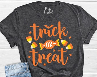 Könnte beinhalten: Ein dunkelgraues T-Shirt mit dem Text "trick or treat" in orangefarbenen Buchstaben. Der Text ist von kleinen orangefarbenen und weißen Candy-Corn-Grafiken umgeben.