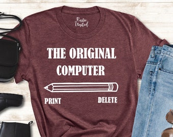 Op de afbeelding: Een maroon t-shirt met de tekst "THE ORIGINAL COMPUTER" en een potloodgrafiek met de woorden "PRINT" en "DELETE" eronder.