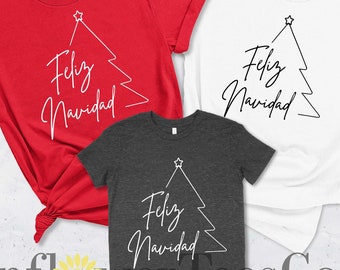 Puede incluir: Tres camisetas con un contorno blanco de un árbol de Navidad y el texto "Feliz Navidad" en blanco. Las camisetas son roja, blanca y gris.