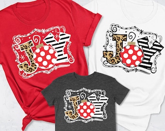 以下が含まれることがあります： クリスマスをテーマにした3枚のTシャツ。"JOY"という単語が、お祝いのデザインで書かれています。"J"はレオパード柄、"O"は赤と白のドット柄のオーナメント、"Y"は黒と白のストライプ柄です。シャツは赤、白、グレーです。
