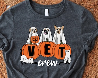 Peut inclure: T-shirt gris avec un motif sur le thème d'Halloween représentant trois chiens habillés en fantômes et des citrouilles avec le texte "VET crew".