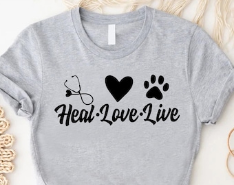 May include: Grey t-shirt with a stethoscope, heart, and paw print graphic. The text "Heal-Love-Live" is printed below the graphic.