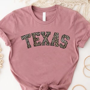 May include: A mauve t-shirt with a leopard print "TEXAS" graphic.