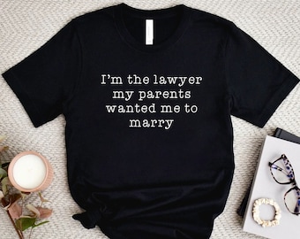 May include: Black t-shirt with white text that reads "I'm the lawyer my parents wanted me to marry".