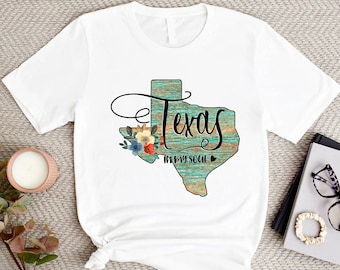 May include: White t-shirt with a graphic of the state of Texas in teal and brown with the words "Texas in my soul" and a small heart.