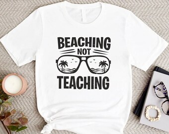 May include: White t-shirt with black text that reads "Beaching Not Teaching" and a graphic of sunglasses with palm trees reflected in the lenses.