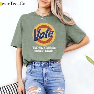 May include: Green t-shirt with a white circle and the word "Vote" in blue letters. The circle has a yellow outer ring and a red inner ring. The text below the circle says "Removes Stubborn Orange Stains".