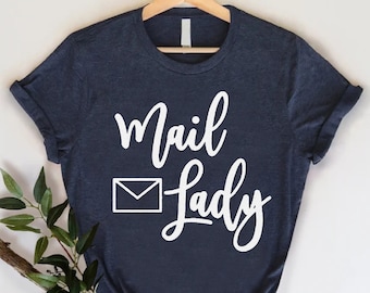 May include: A navy blue t-shirt with a white envelope graphic and the text "Mail Lady" in white cursive lettering.