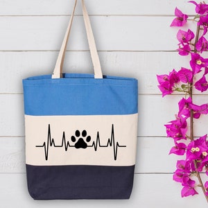 May include: A blue, white, and navy blue striped tote bag with a black paw print heartbeat graphic. The bag has a canvas texture and two handles.