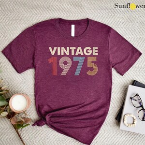 May include: A maroon t-shirt with the text "Vintage 1975" in a retro font with colorful stripes.