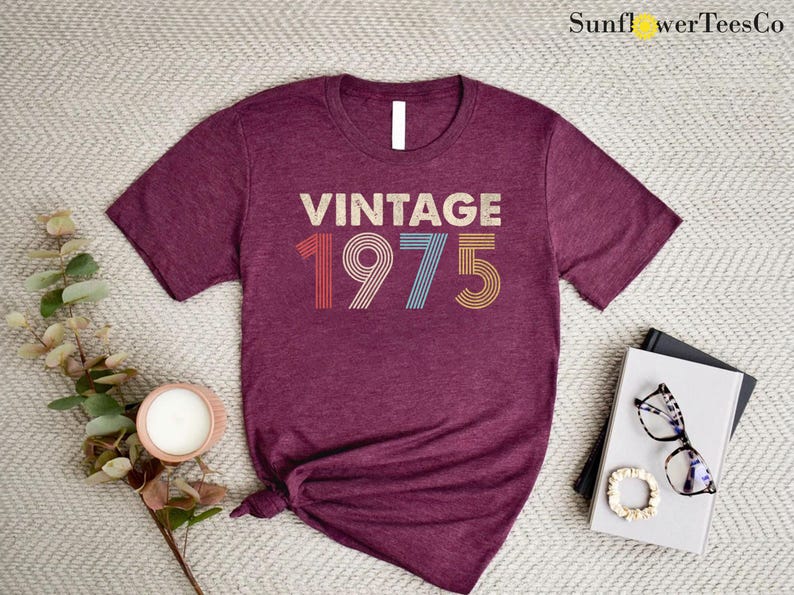 May include: A maroon t-shirt with the text "Vintage 1975" in a retro font with colorful stripes.