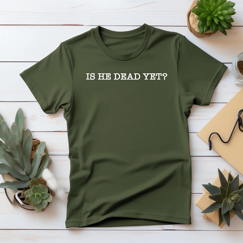 K&ouml;nnte beinhalten: Ein gr&uuml;nes T-Shirt mit dem Aufdruck "IS HE DEAD YET?" in wei&szlig; auf der Vorderseite.