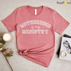 May include: A dusty rose colored t-shirt with the text "MOTHERHOOD is my MINISTRY" in white.