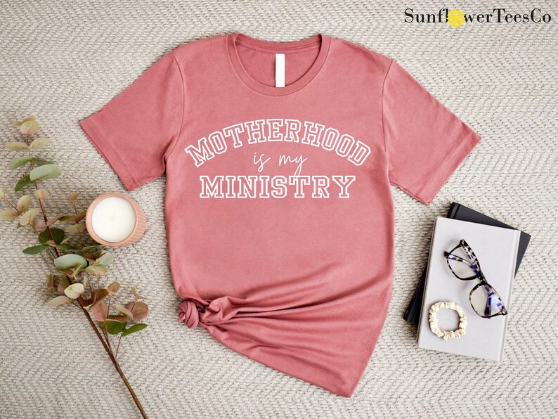 May include: A dusty rose colored t-shirt with the text "MOTHERHOOD is my MINISTRY" in white.