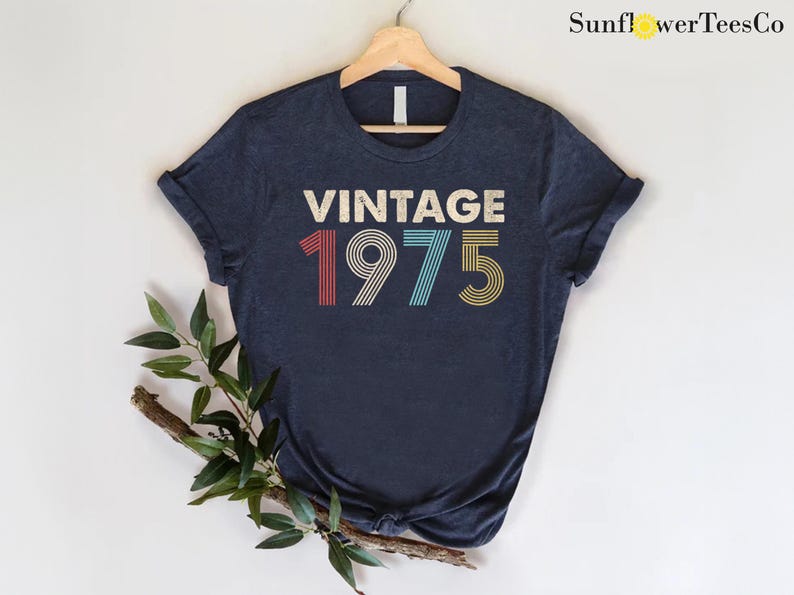 May include: A navy blue t-shirt with the text "Vintage 1975" in a retro font with colorful stripes.