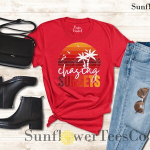 May include: Red t-shirt with a vintage sunset graphic and the text "chasing sunsets". The shirt is paired with blue jeans, black boots, and a black purse.