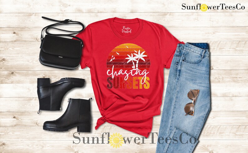 May include: Red t-shirt with a vintage sunset graphic and the text "chasing sunsets". The shirt is paired with blue jeans, black boots, and a black purse.