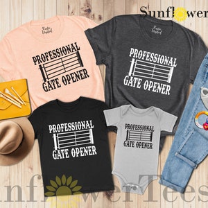 Op de afbeelding: Een set van vier t-shirts met een zwart-witte afbeelding van een poort met de tekst "Professional Gate Opener". De shirts zijn in verschillende kleuren, waaronder roze, grijs, zwart en lichtgrijs. De shirts zijn gerangschikt op een houten oppervlak met een spijkerbroek, een hoed en een handtas.